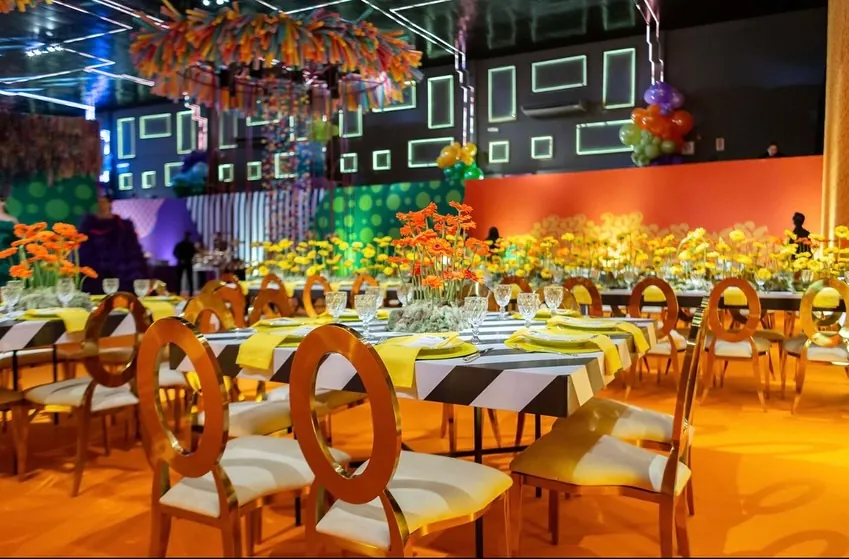 Salão da Luna Live decorado para festa, com cadeiras douradas, mesas postas e arranjos de flores